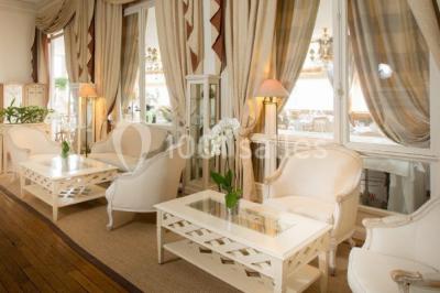 Deux tables de massage recouvertes de draps beiges, avec une vue sur un paysage urbain et verdoyant à travers une fenêtre.