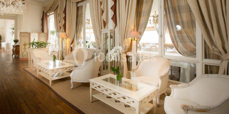 Salon élégant avec fauteuils blancs, tables basses en verre, rideaux beiges et parquet en bois.