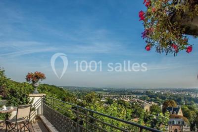Deux tables de massage recouvertes de draps beiges, avec une vue sur un paysage urbain et verdoyant à travers une fenêtre.