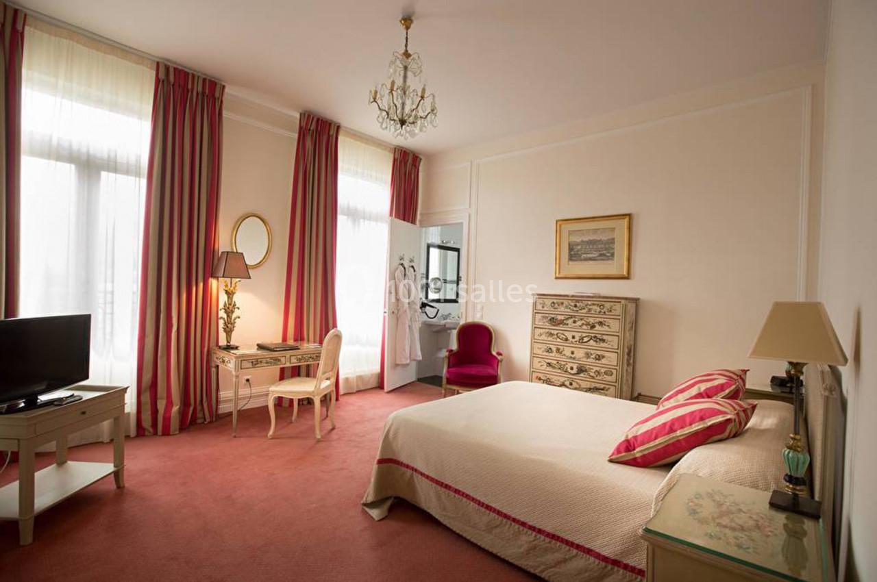 Chambre lumineuse avec lit double, bureau, fauteuil, commode et rideaux rayés, décorée dans un style classique.