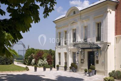 Deux tables de massage recouvertes de draps beiges, avec une vue sur un paysage urbain et verdoyant à travers une fenêtre.