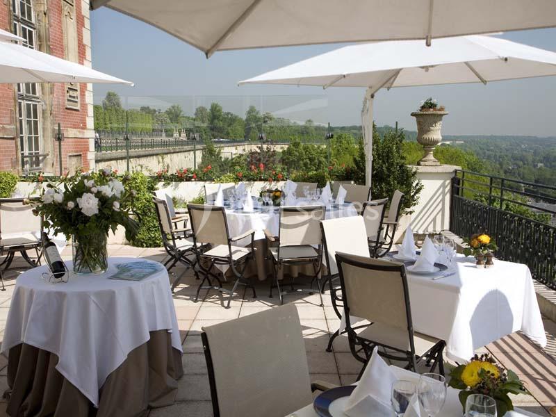 Terrasse d'un restaurant avec tables dressées, parasols blancs et vue sur un paysage verdoyant en arrière-plan.