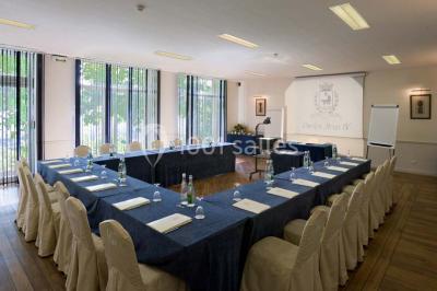 Deux tables de massage recouvertes de draps beiges, avec une vue sur un paysage urbain et verdoyant à travers une fenêtre.