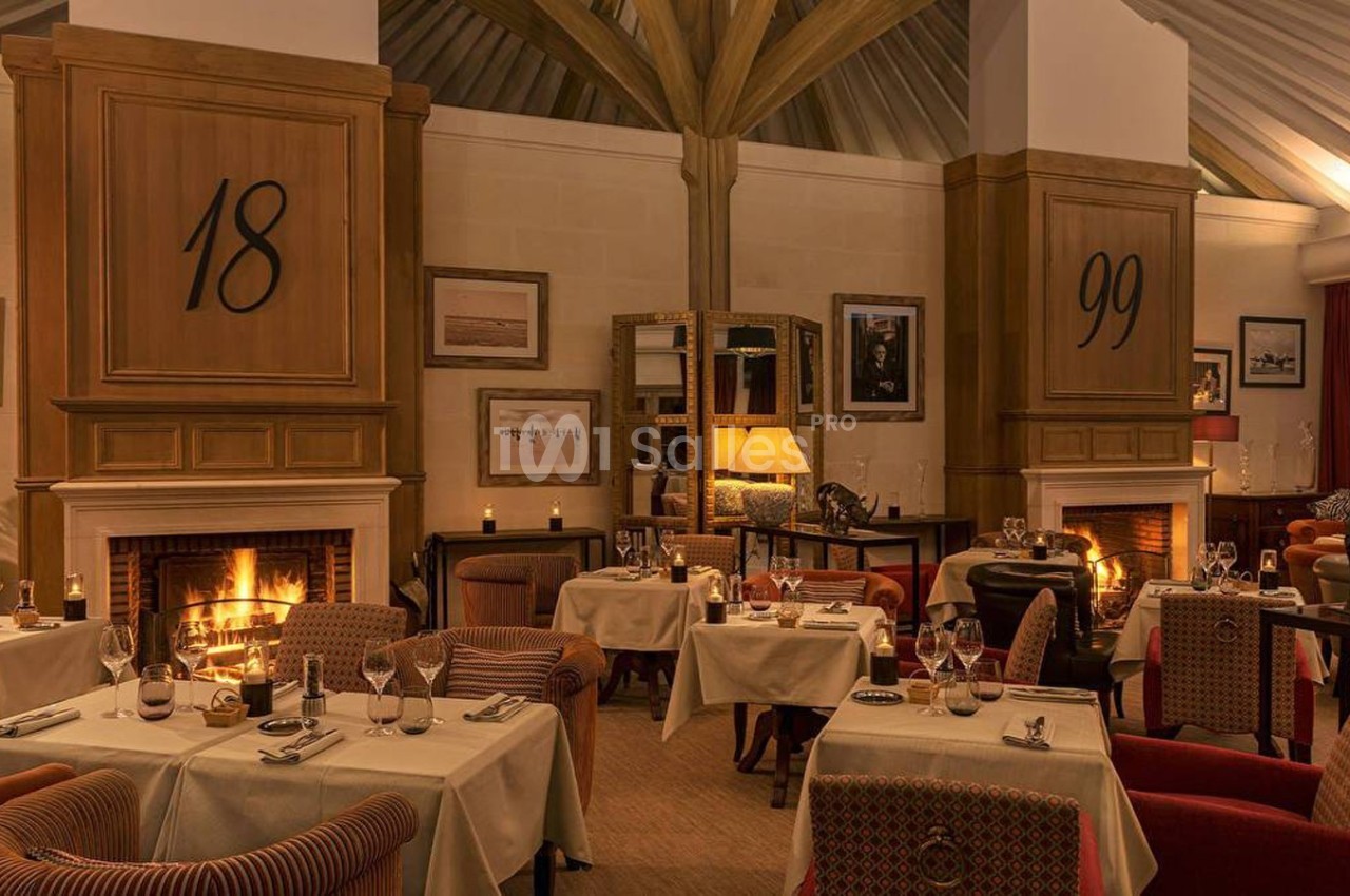 Salle de restaurant élégante avec tables dressées, cheminées allumées et éclairage chaleureux.