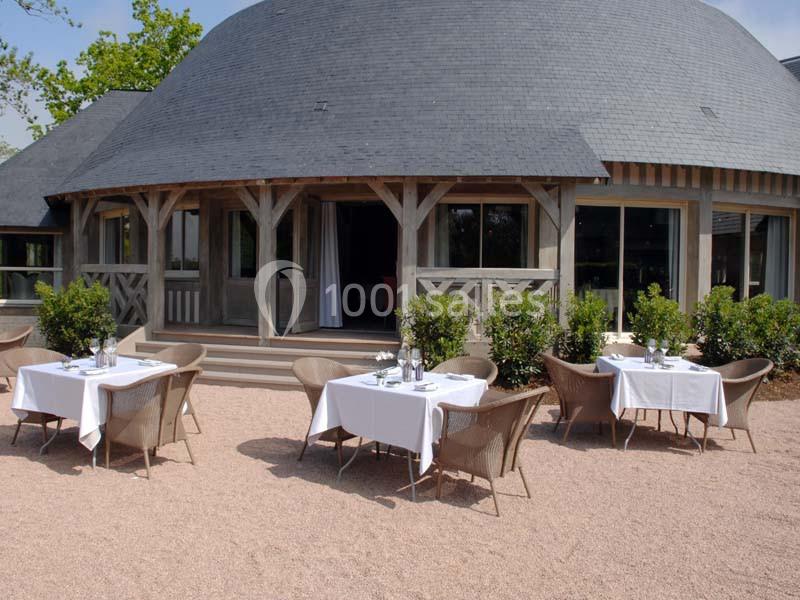 Terrasse d'un restaurant avec tables dressées, chaises en osier et façade en bois sous un toit ardoisé.