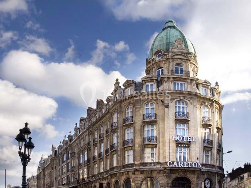Façade d'un hôtel historique avec dôme vert, architecture classique, ciel bleu et lampadaire au premier plan.
