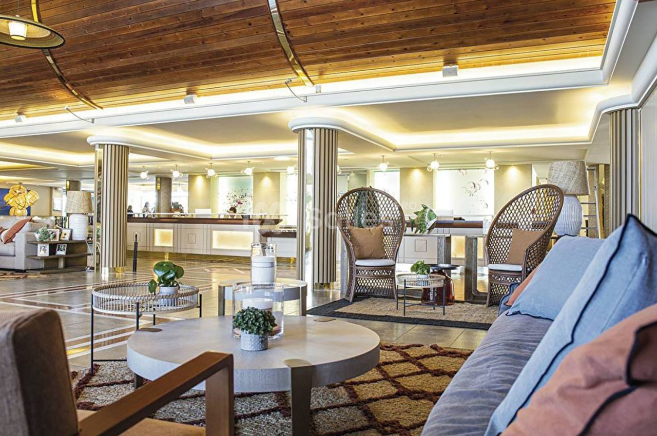 Espace intérieur lumineux avec mobilier moderne, fauteuils en rotin, tables basses et plafond en bois.