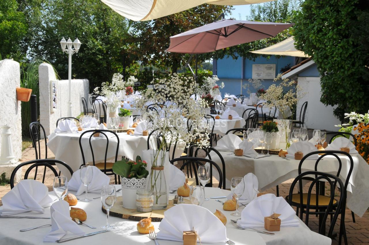 Terrasse d'un restaurant avec des tables dressées, nappes blanches, serviettes pliées et décorations florales.