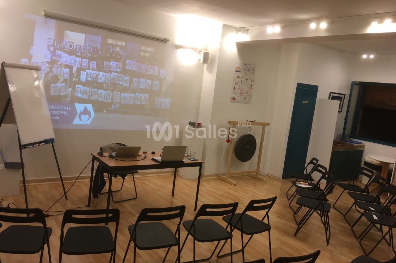 Salle de réunion avec chaises pliantes, tableau blanc, gong et projection sur un mur.