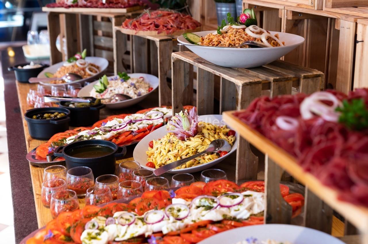 Buffet varié avec salades, charcuteries, tomates, mozzarella et condiments disposés sur des caisses en bois.