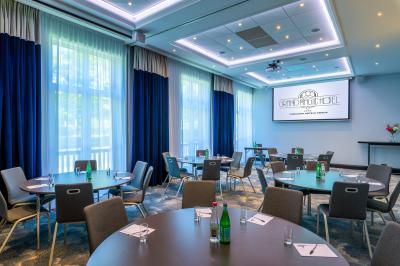 Salle de conférence lumineuse avec rangées de chaises alignées, écran de projection et portes vitrées au fond.