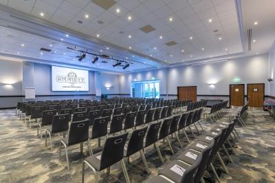 Salle de conférence lumineuse avec rangées de chaises alignées, écran de projection et portes vitrées au fond.