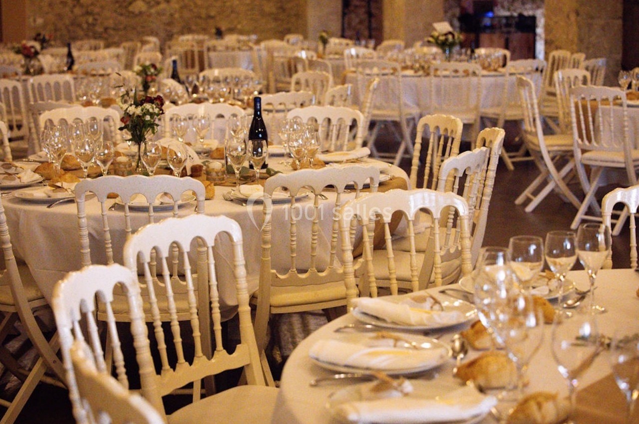 Salle de réception avec tables rondes dressées, nappes blanches, chaises en bois clair et décoration florale.