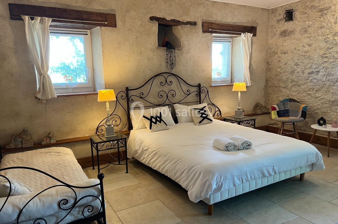 Chambre avec lit double, lit simple, murs en pierre, fenêtres lumineuses et décoration rustique.