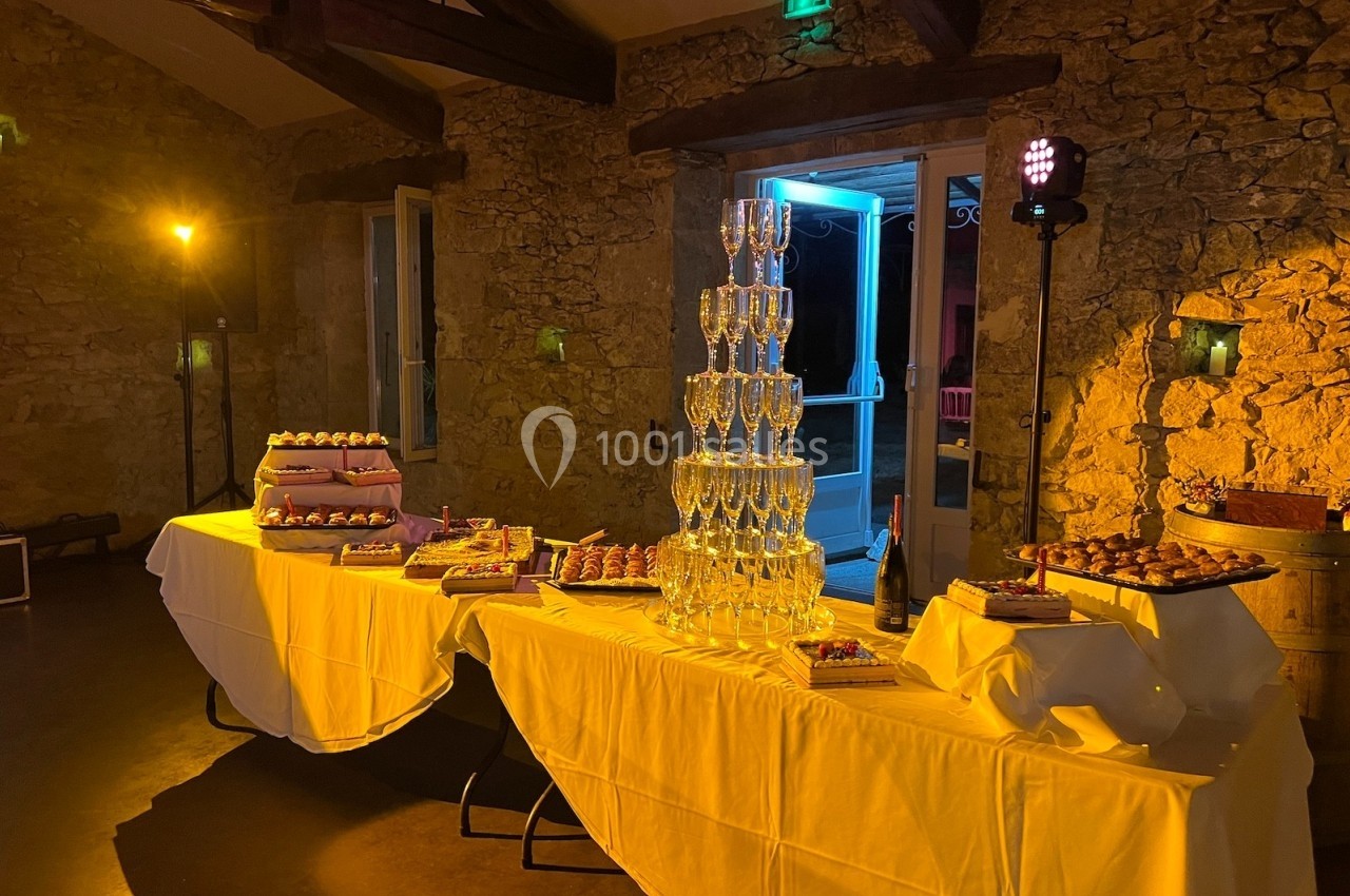 Tables décorées avec des nappes blanches, une pyramide de flûtes à champagne et des desserts dans une salle en pierre…