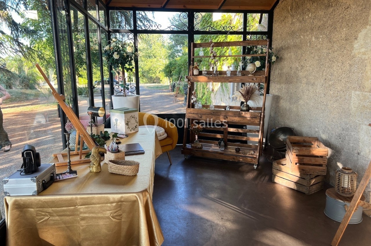Espace décoré avec une table recouverte d'une nappe dorée, étagères en bois et éléments rustiques près d'une baie vitrée.
