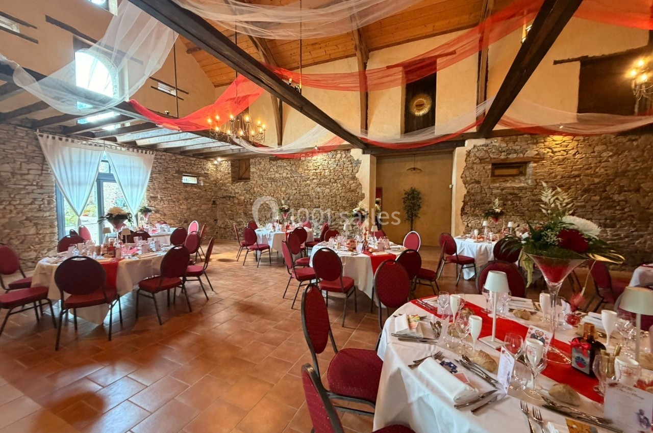 Salle de réception décorée avec des tables rondes dressées, des chaises rouges et des voilages suspendus au plafond.