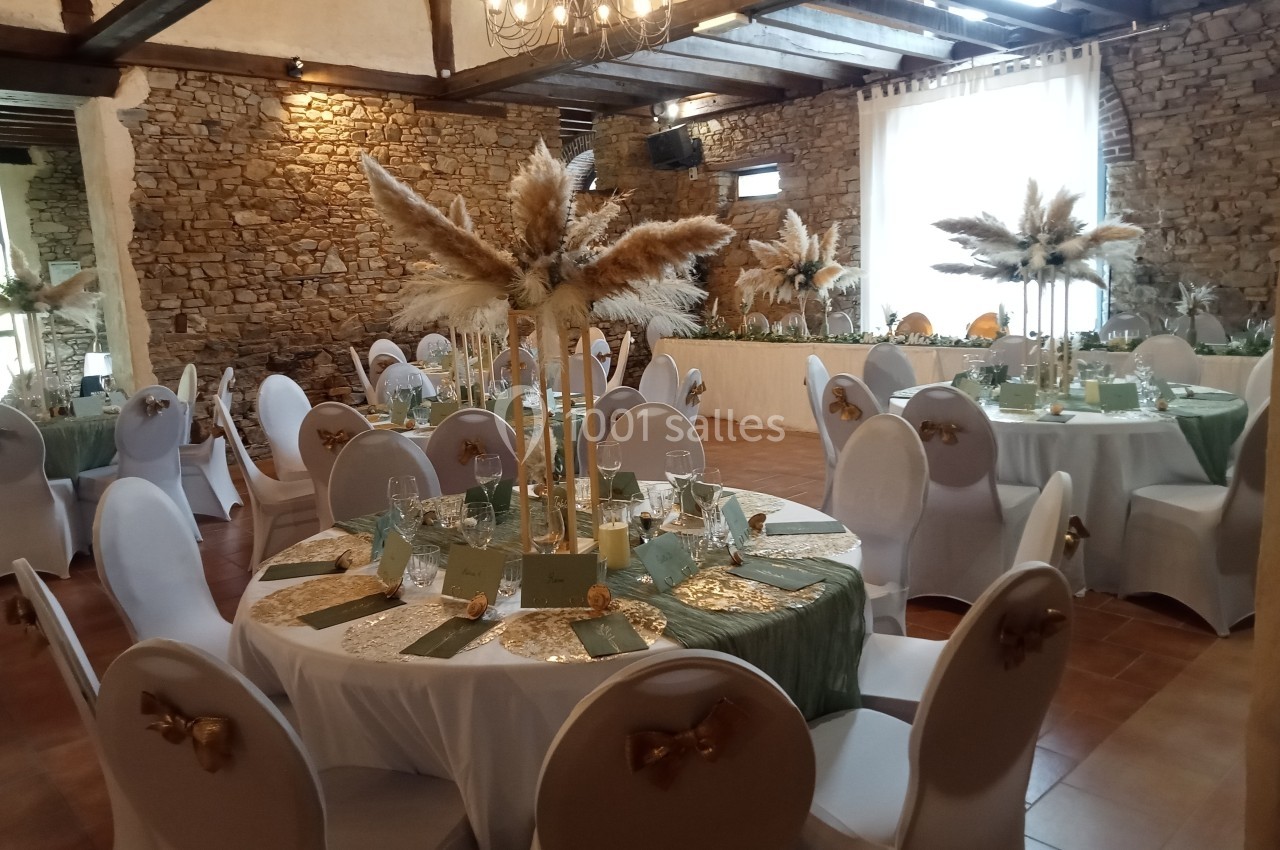 Salle de réception décorée avec des tables rondes, nappes blanches, centres de table en pampas et chaises ornées de nœuds…