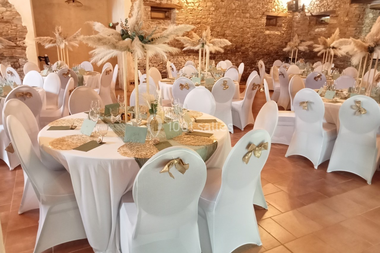 Salle de réception décorée pour un événement, avec des tables rondes, nappes blanches et centres de table en pampas.