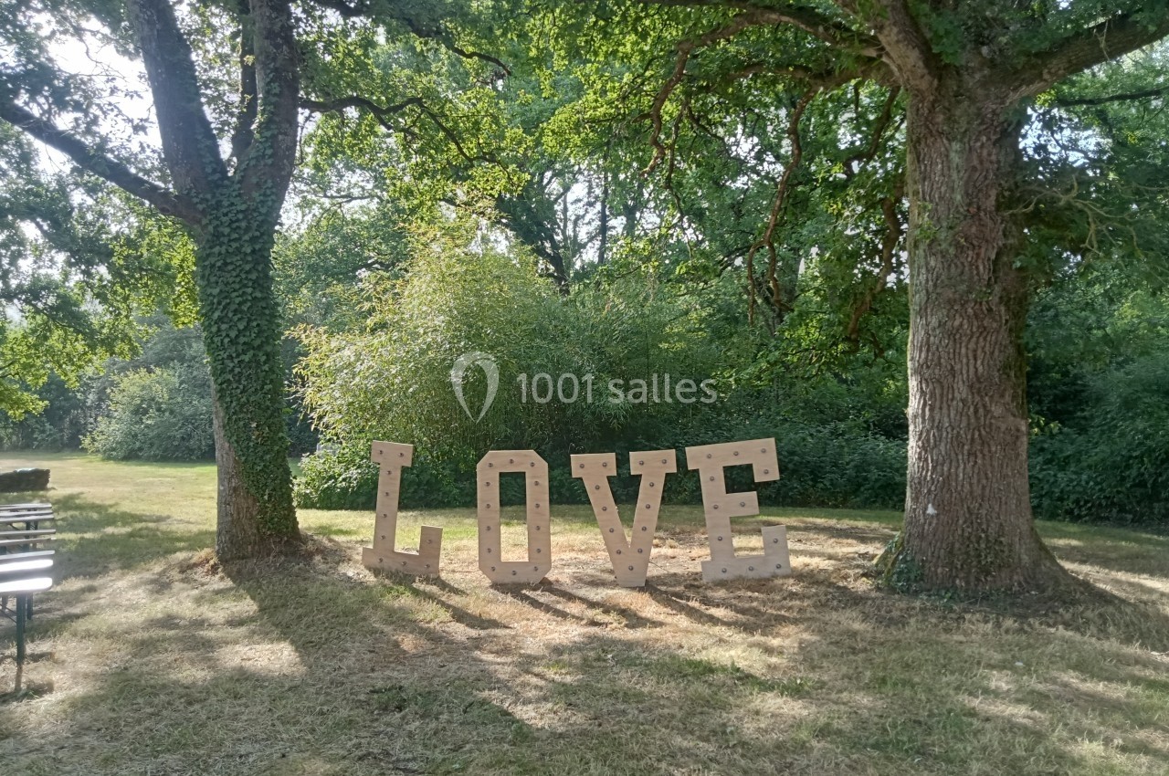 Lettres géantes formant le mot ’LOVE’ installées entre deux arbres dans un espace vert ensoleillé.