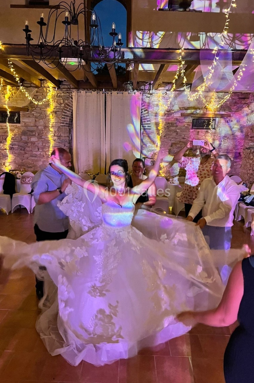 Une mariée danse au centre d'une salle décorée de guirlandes lumineuses, entourée d'invités.