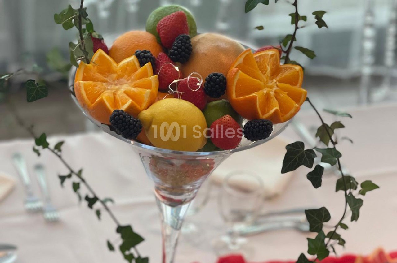 Coupe en verre garnie de fruits frais variés, dont oranges, citron, baies et feuilles de lierre décoratives.