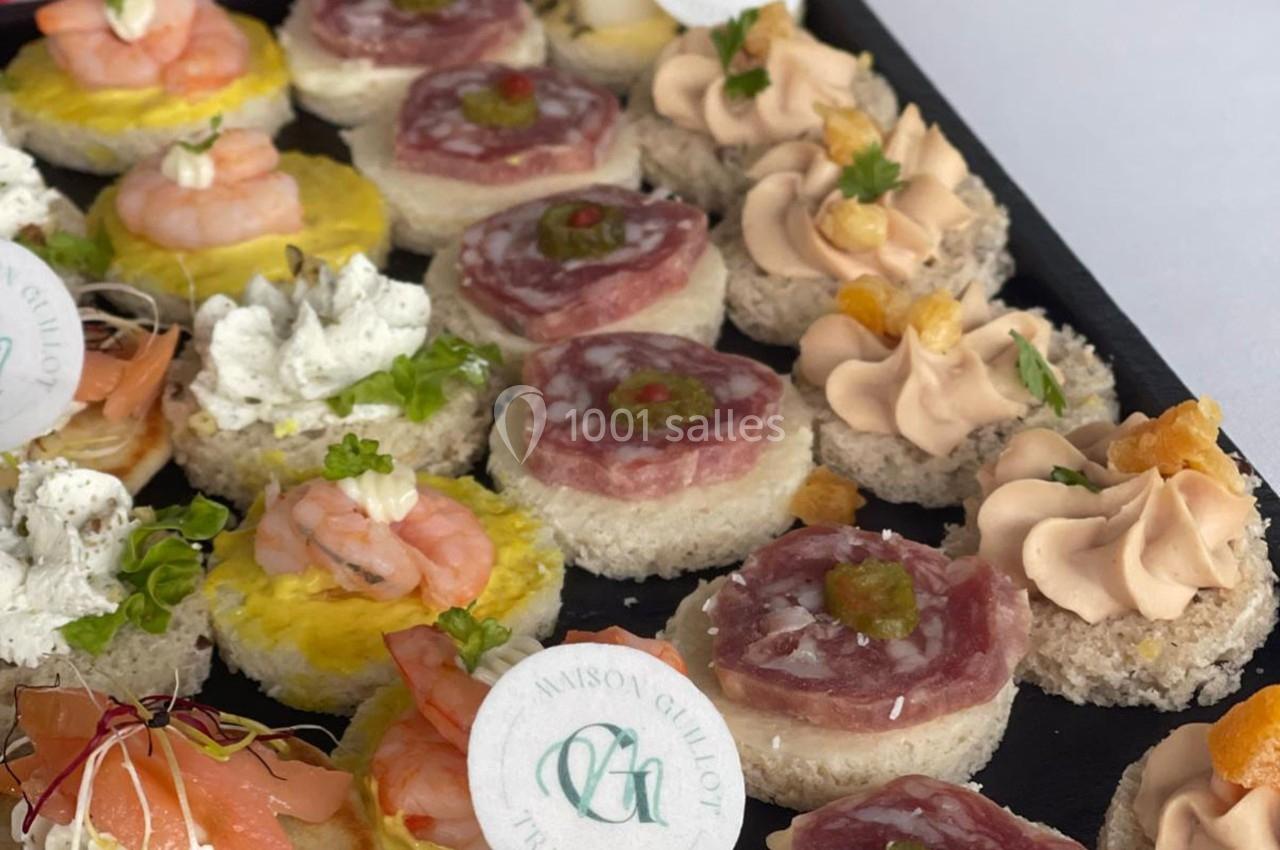 Plateau de canapés variés avec crevettes, saumon, mousse et charcuterie, décorés de garnitures fraîches.