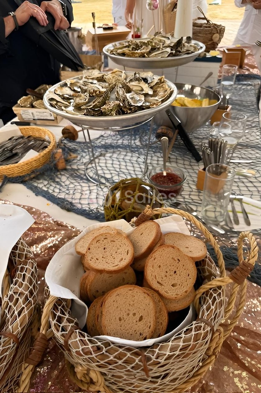 Plateau d'huîtres et paniers de pain grillé disposés sur une table décorée avec un filet de pêche.