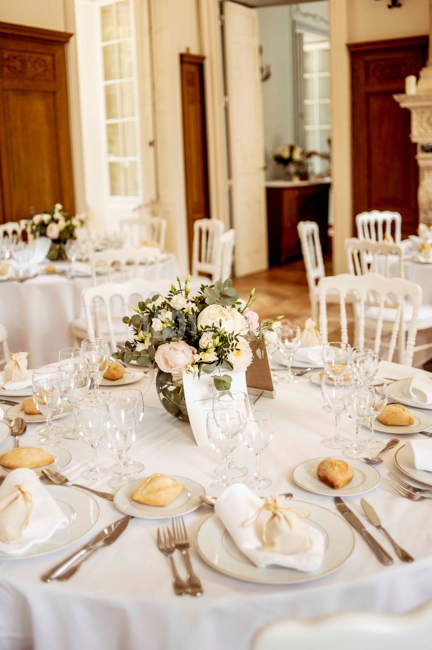 Salle de réception élégante avec tables dressées, nappes blanches, vaisselle raffinée et centre de table floral.