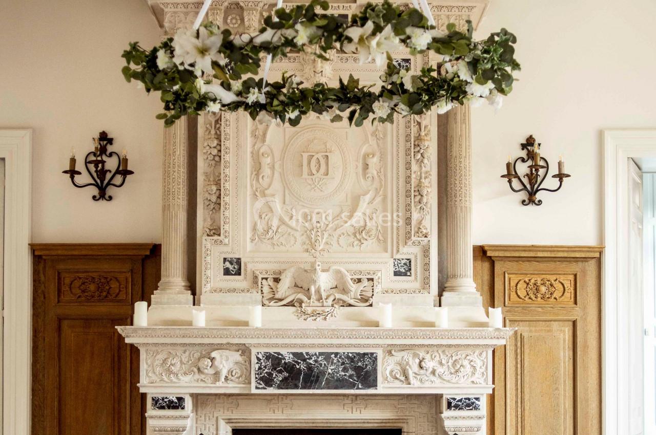 Cheminée sculptée ornée de détails classiques, surmontée d'un lustre floral suspendu, avec table dressée au premier plan.
