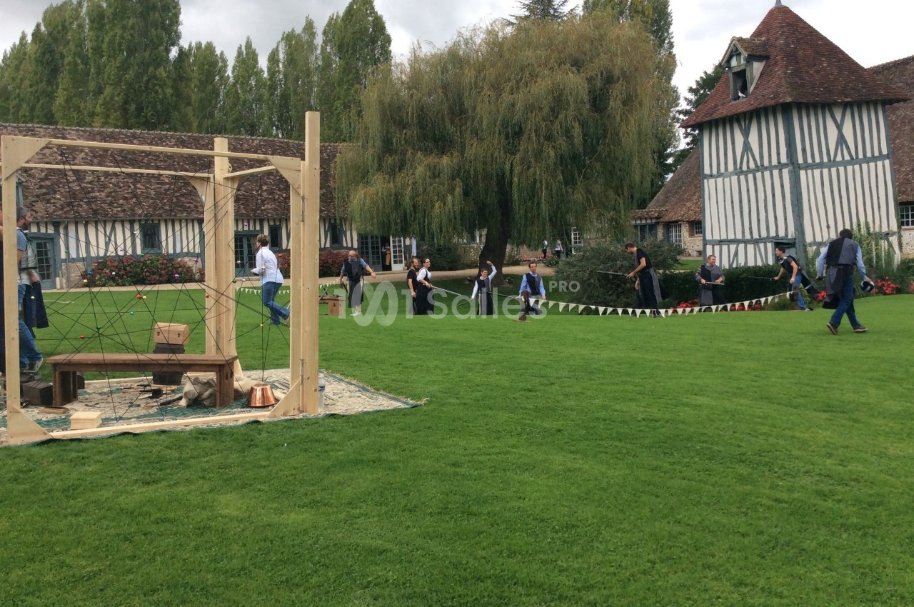 Personnes participant à une activité en plein air sur une pelouse, près de bâtiments à colombages et d'arbres.