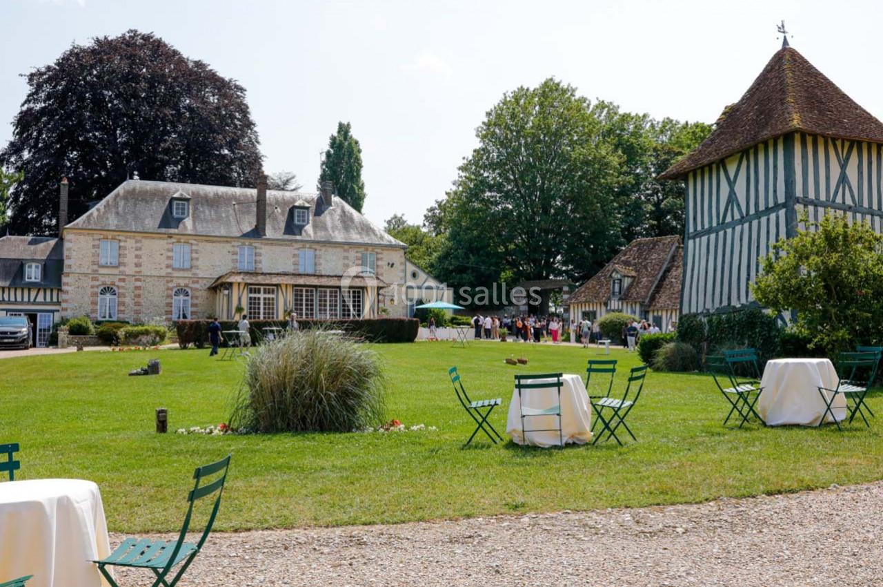 Jardin avec tables et chaises disposées devant un manoir en pierre et une construction à colombages.
