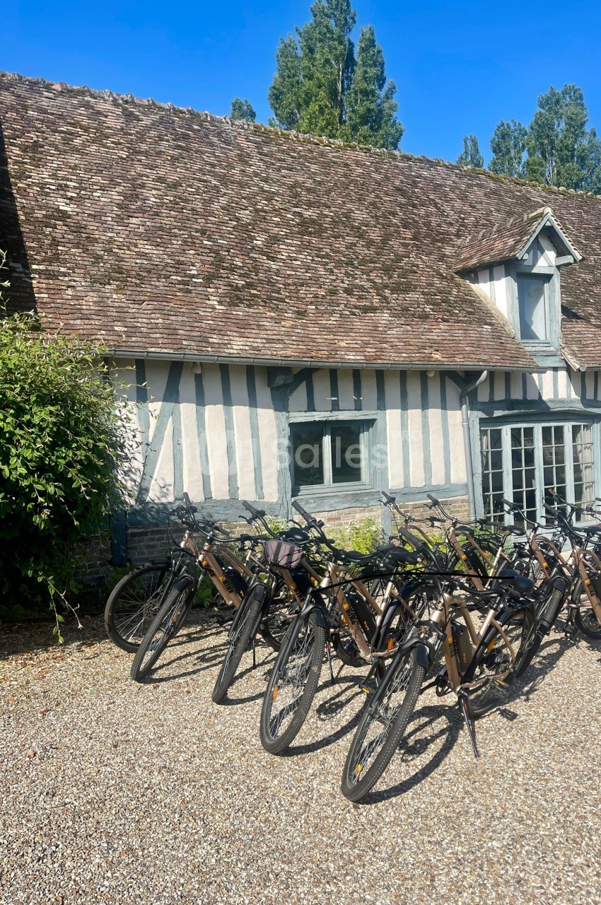 Alignement de vélos électriques devant une maison à colombages avec un toit en tuiles, entourée de végétation.