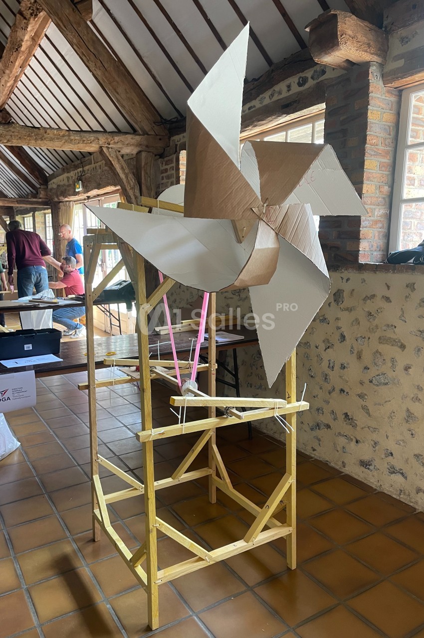 Maquette d'une éolienne en carton et bois exposée dans une salle avec murs en pierre et poutres apparentes.