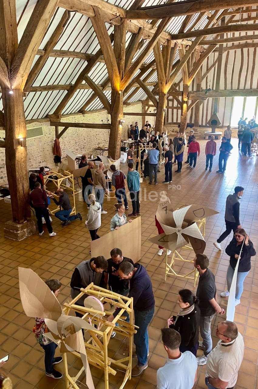 Des personnes participent à un atelier collaboratif dans une grande salle avec charpente en bois et sol en carreaux.