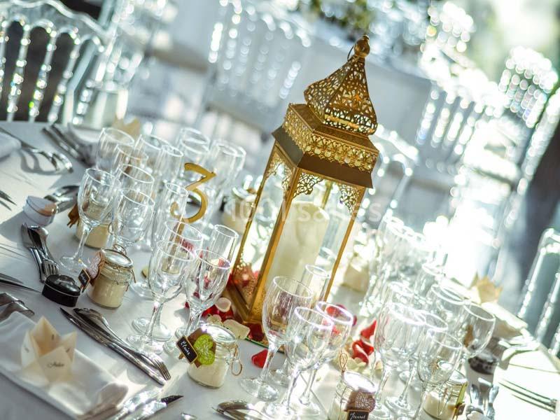 Table élégamment dressée avec une lanterne dorée au centre, entourée de verres, couverts et décorations.