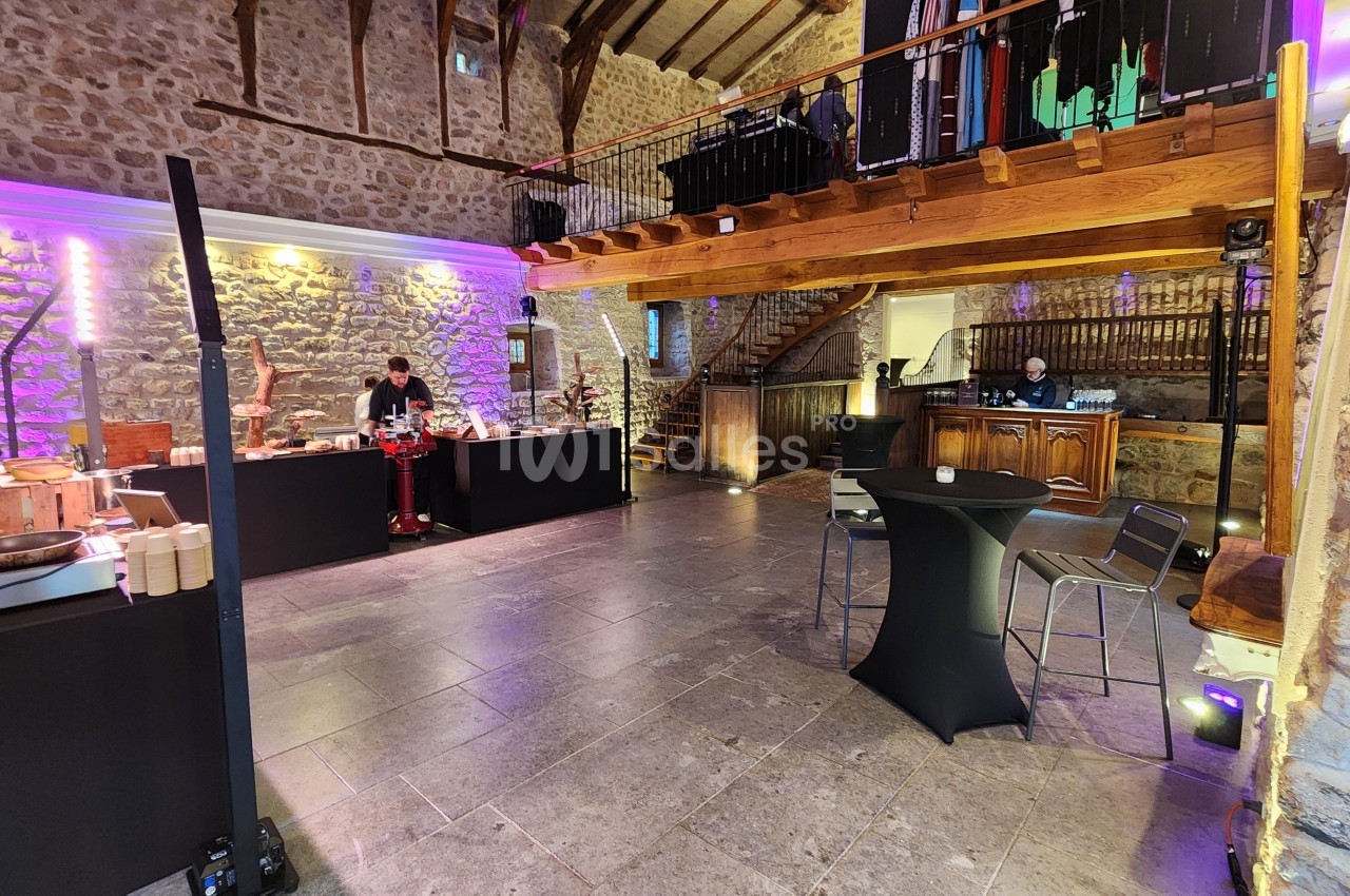 Salle en pierre avec éclairage coloré, tables hautes et espace buffet, ambiance événementielle chaleureuse.