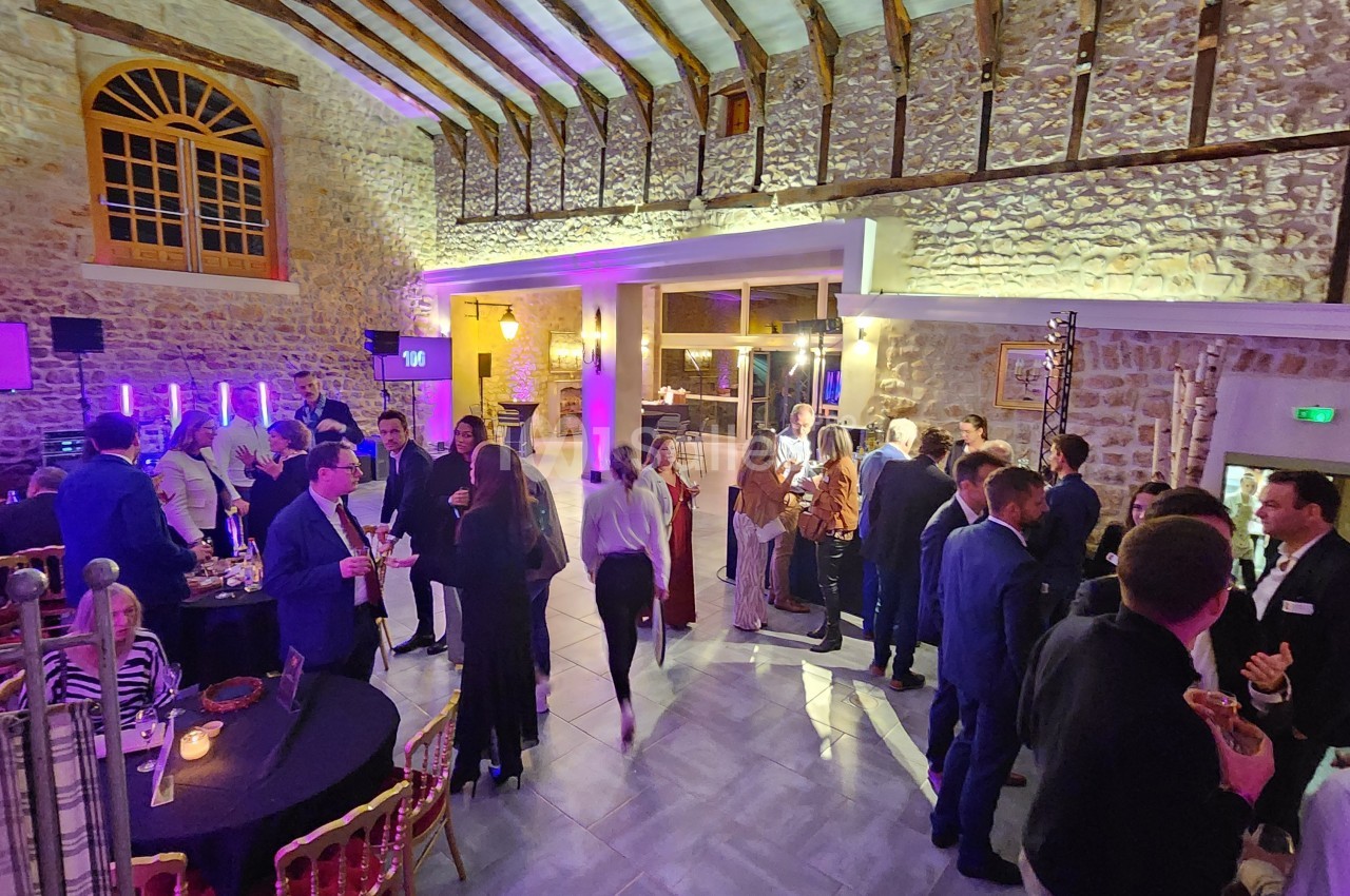 Salle en pierre avec des invités debout et assis, discutant lors d'un événement festif en soirée.