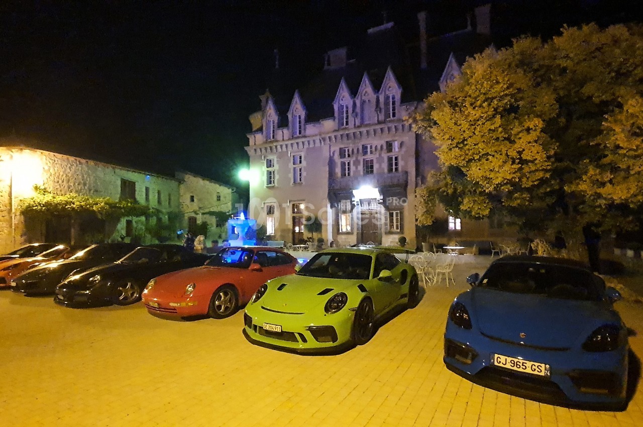 Alignement de voitures sportives colorées stationnées sur une place pavée devant un bâtiment illuminé de nuit.