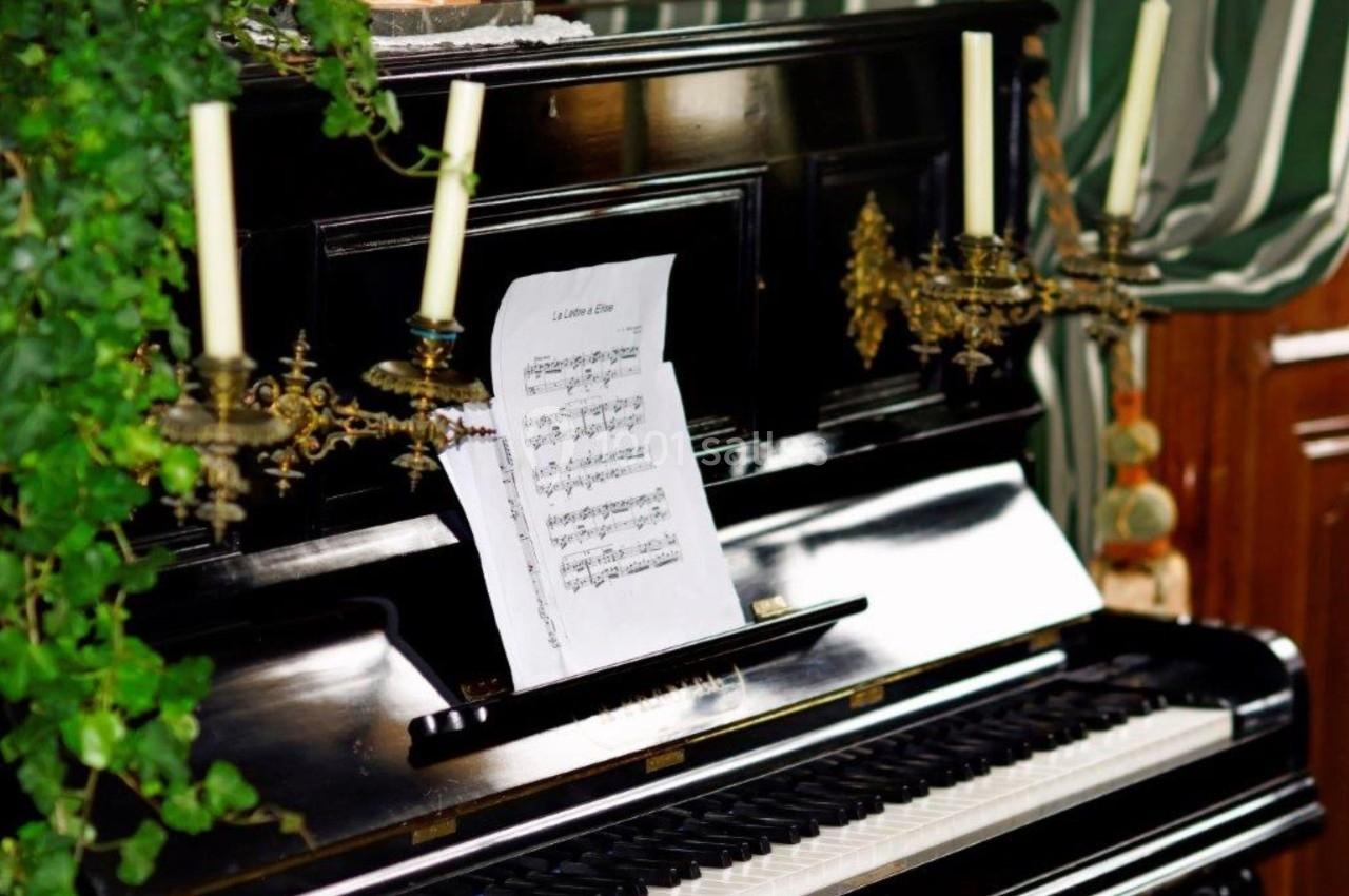 Piano noir avec des partitions posées sur le pupitre, entouré de chandeliers et de plantes décoratives.