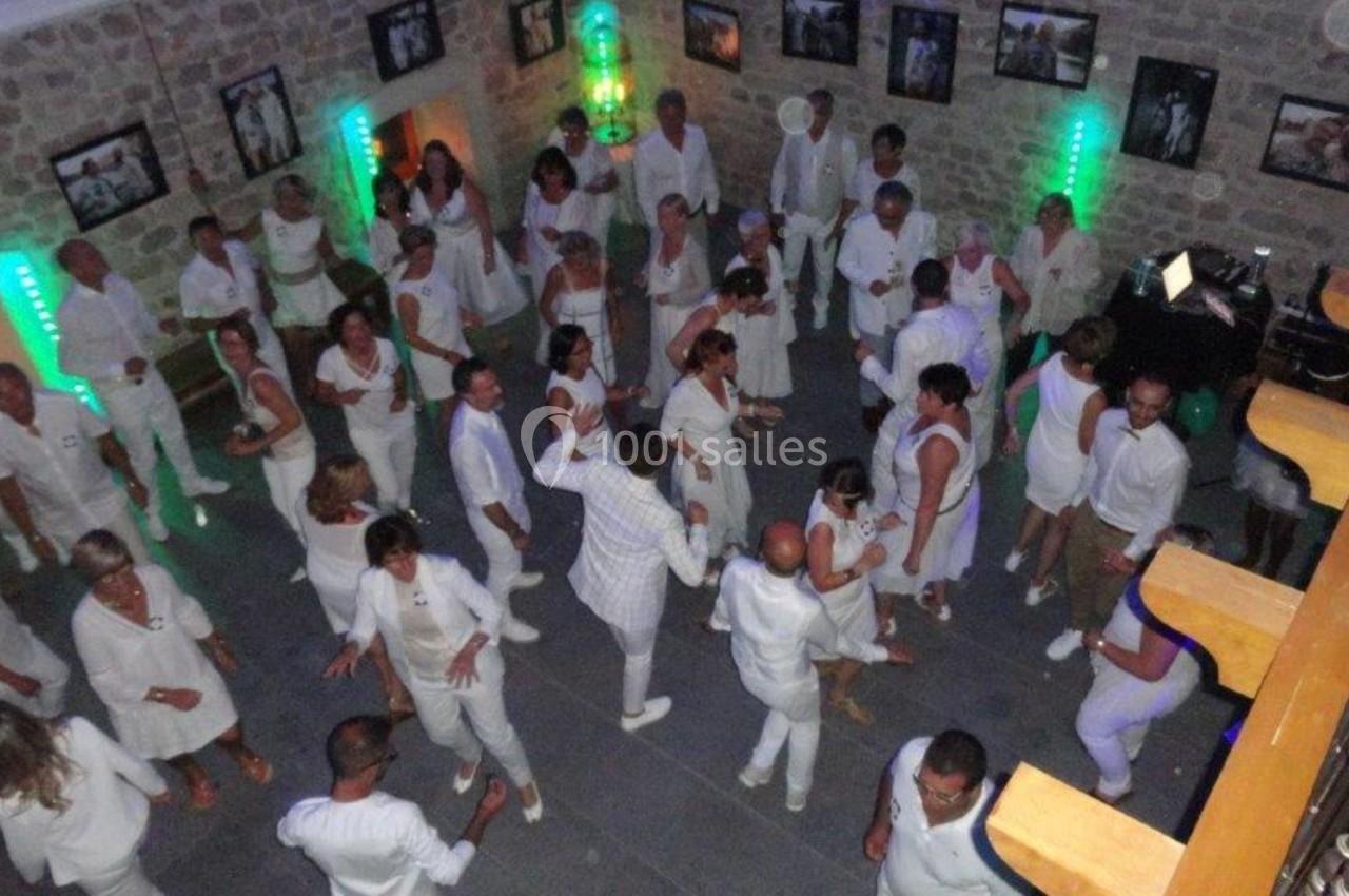 Personnes vêtues de blanc dans une salle en pierre, dansant sous des lumières colorées.