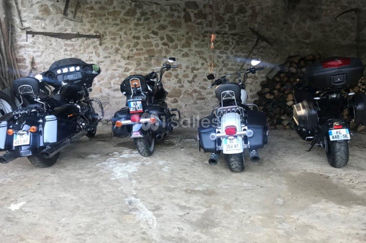 Quatre motos garées côte à côte dans un abri en pierre, avec des accessoires et bagages installés à l'arrière.