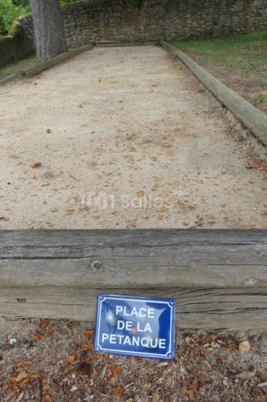 Terrain de pétanque en sable délimité par des bordures en bois, avec un panneau indiquant ’Place de la pétanque’.