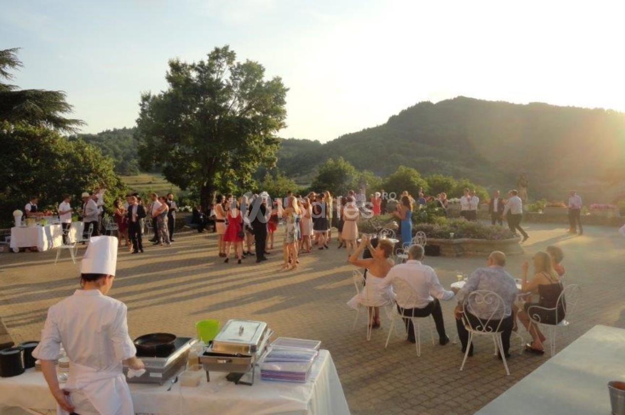 Groupe de personnes réunies en extérieur lors d'une réception au coucher du soleil, avec un chef cuisinant au premier plan.