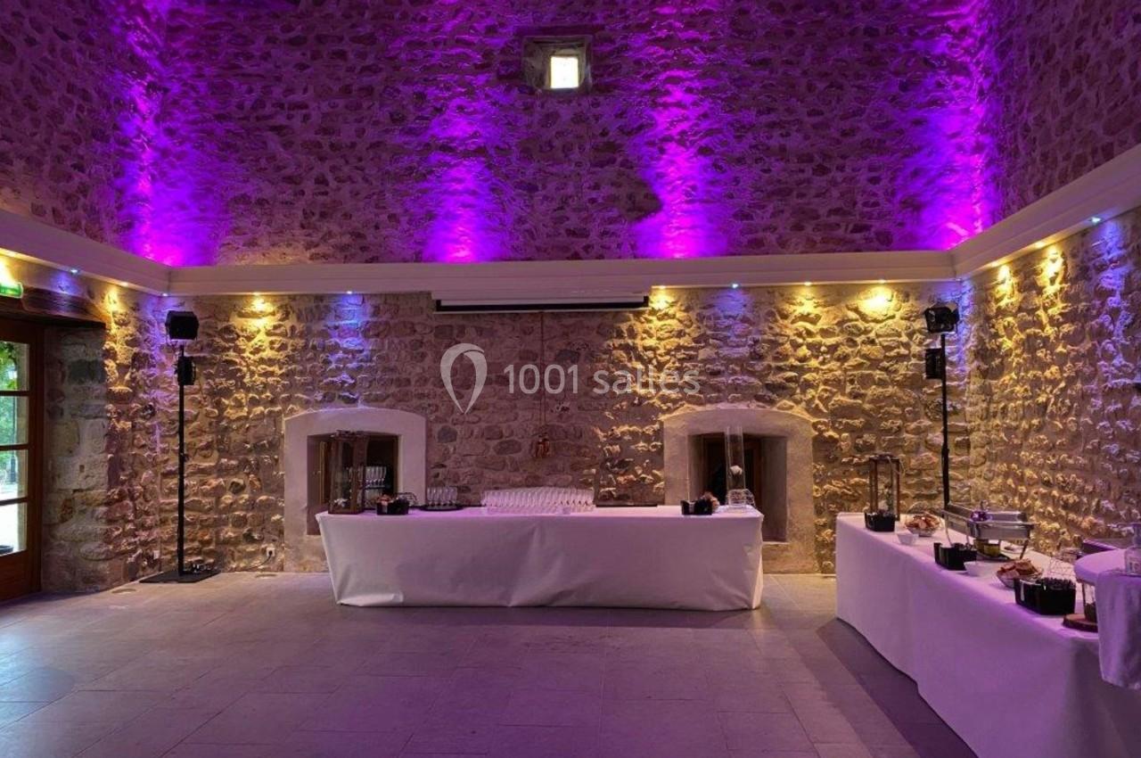 Salle en pierre avec éclairage violet, tables dressées avec nappes blanches et éléments de buffet.