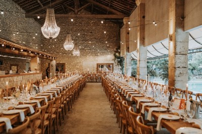 Salle en pierre avec une grande cheminée, table ronde dressée avec chaises rembourrées et bouteilles d'eau.