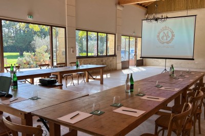 Salle en pierre avec une grande cheminée, table ronde dressée avec chaises rembourrées et bouteilles d'eau.