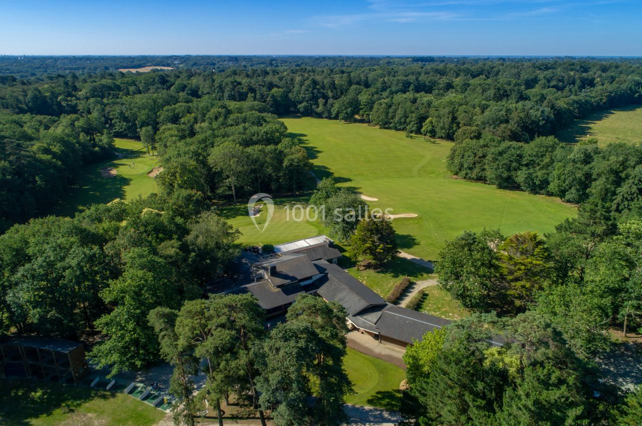Vue aérienne d'un terrain de golf entouré de forêt avec un bâtiment principal au centre.