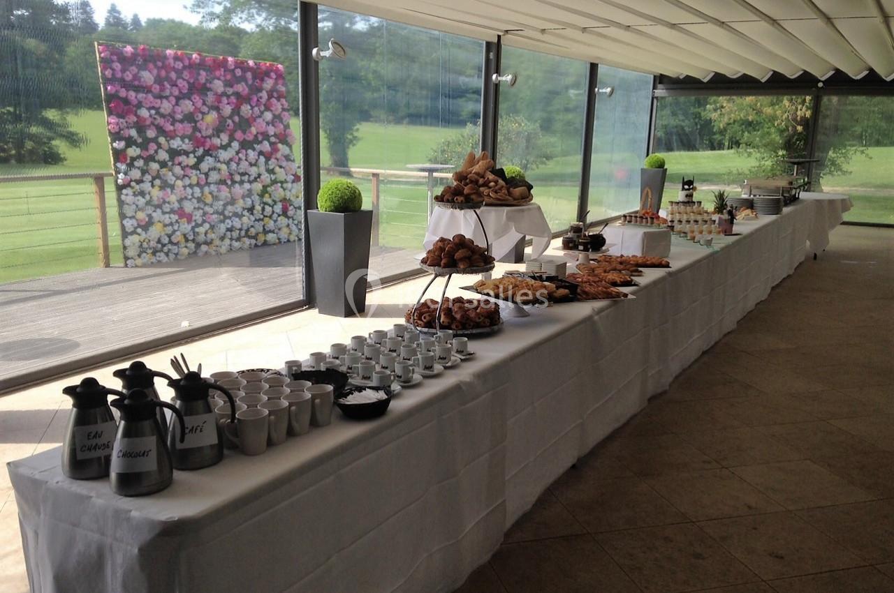 Buffet disposé sur une longue table avec viennoiseries, boissons chaudes et décor floral en arrière-plan.