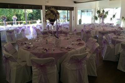 Salle de réception décorée pour un mariage, avec des tables rondes dressées, nappes blanches et arrangements floraux.